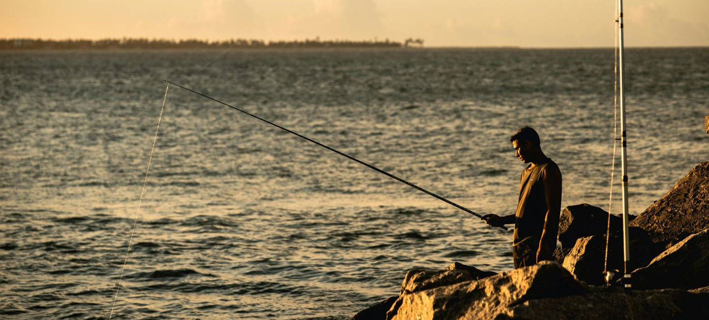 Un hombre pesca sobre las piedras del espigón de una bahía